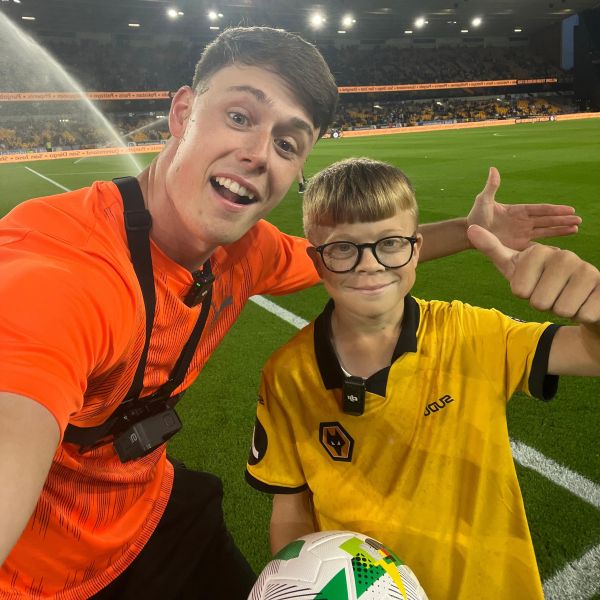 Young man and teen boy pose for a selfie while on a football pitch