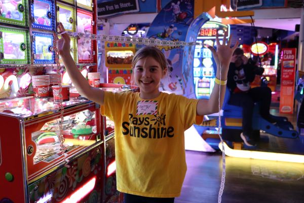 Little girl in yellow Rays of Sunshine t-shirt lifts a strip of tickets aloft while in an arcade