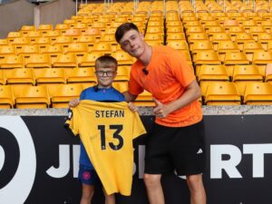 Ten boy and young man smile for a picture, while the young one holds up a yellow football shirt with Stfan 13 on the back