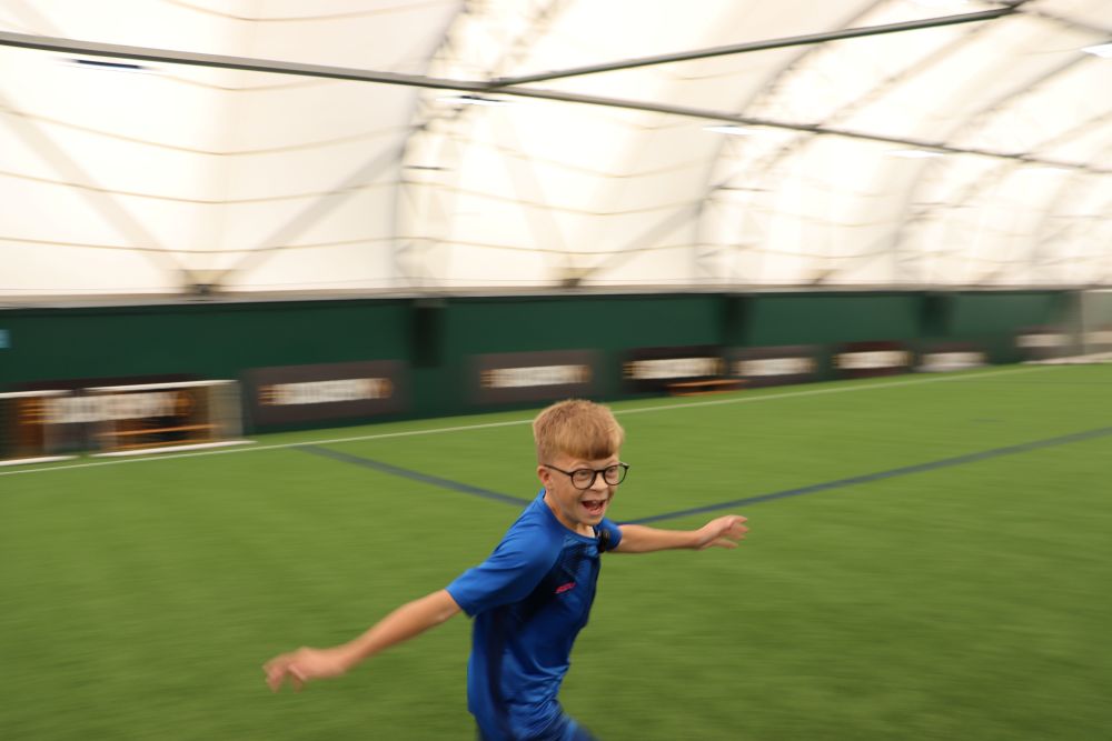 Young teen celebrates scoring a goal by running around an ndoor footall pitch
