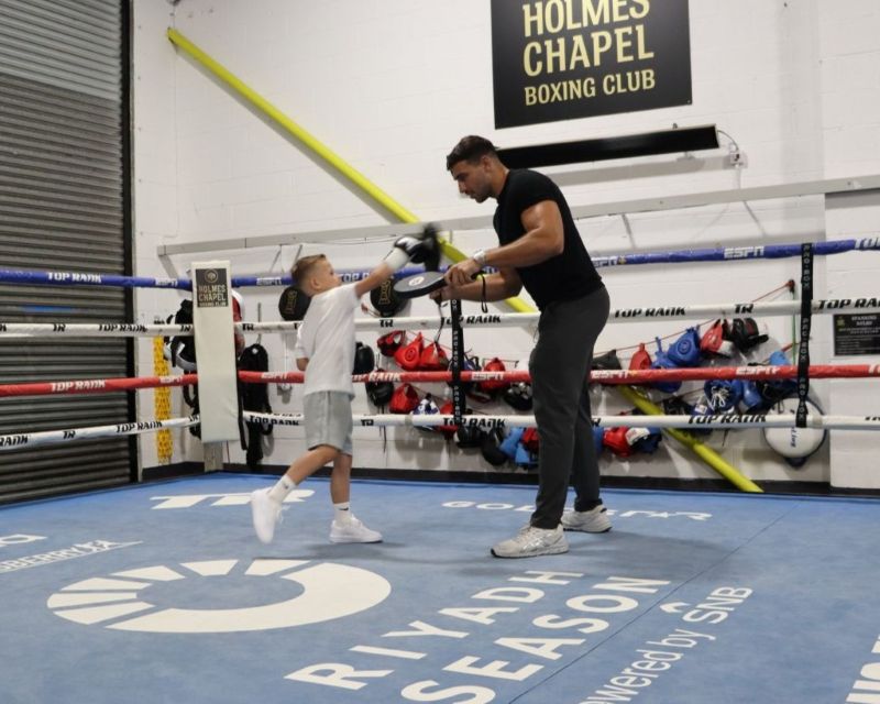 Little boy in a boxing ring with pro boxer, punching a pad