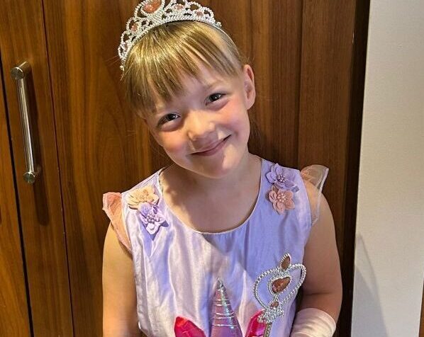 Little girl in princess costume stands and smiles with a magic wand