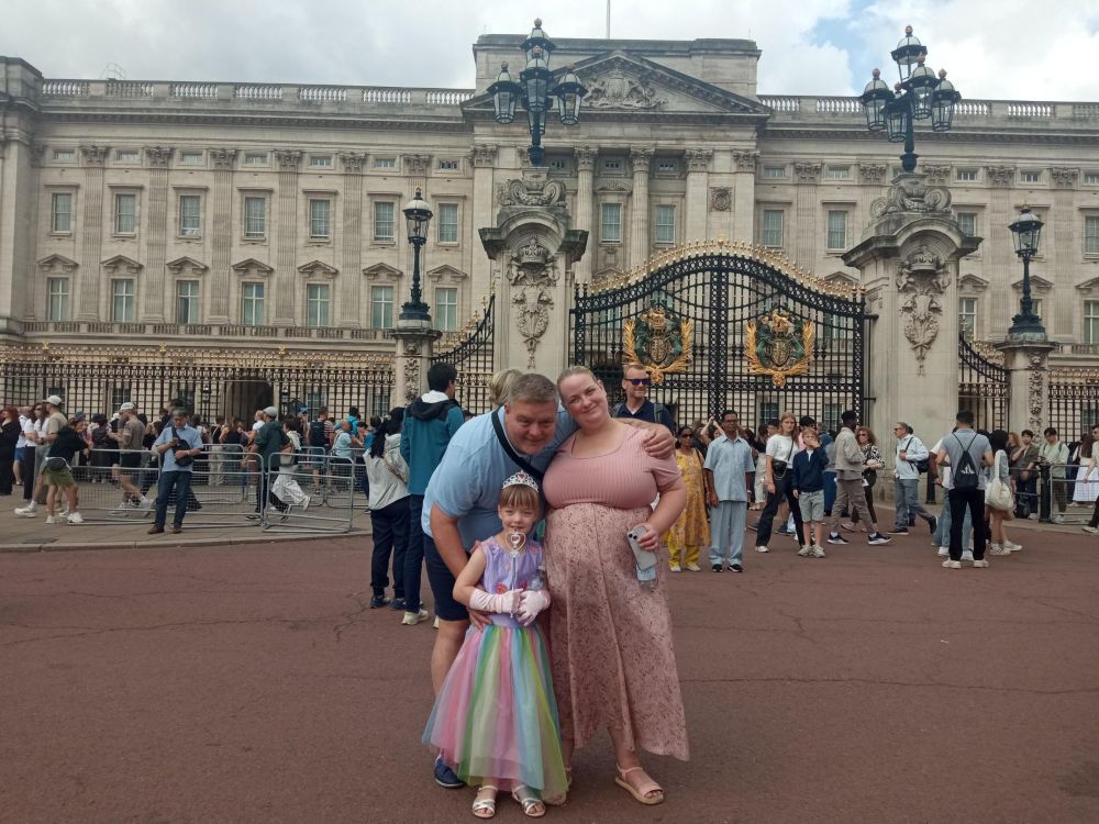 Family (parents and little girl) stand outside Buckingham Palace