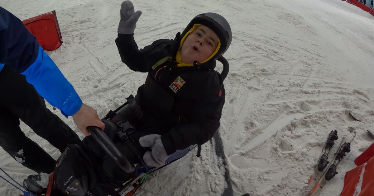 Boy posing for a photo while sat in an adaptive skiing sled while at an indoor ski slope