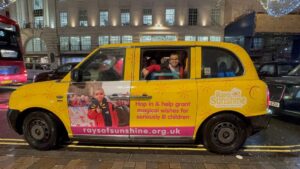 Little boy stands in the back window of a taxi with his picture on it