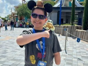 Young teen boy smiles while pointing at a baby yoda plushie on his shoulder